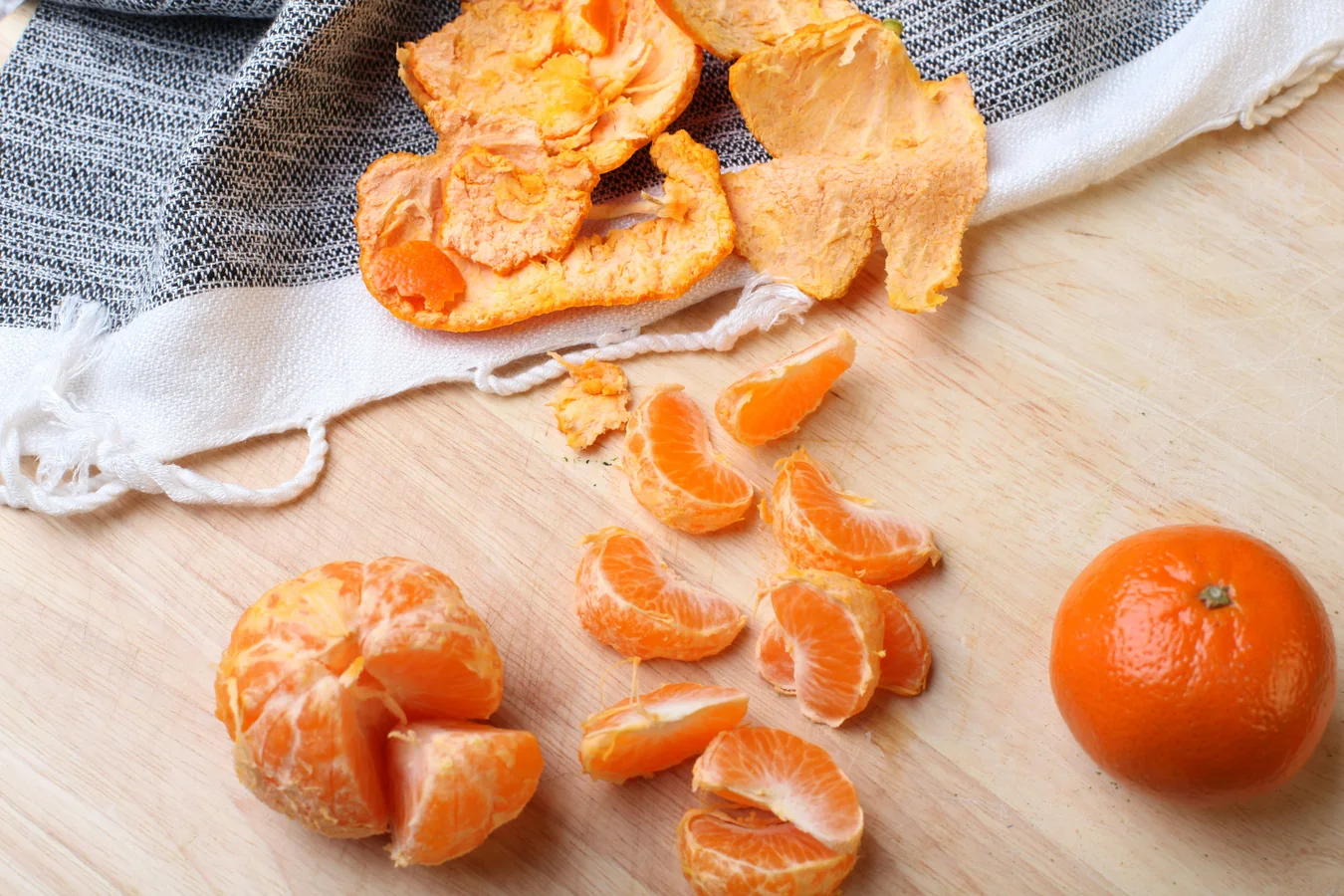 Oljuštene mandarine na svetlom drvenom stolu sa lanenom tkaninom